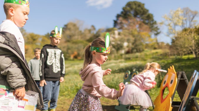 Children wearing bunny ears at Easter in Bodnant Garden, throwing balls through the mouth of different wooden animals including a frog and a chick.